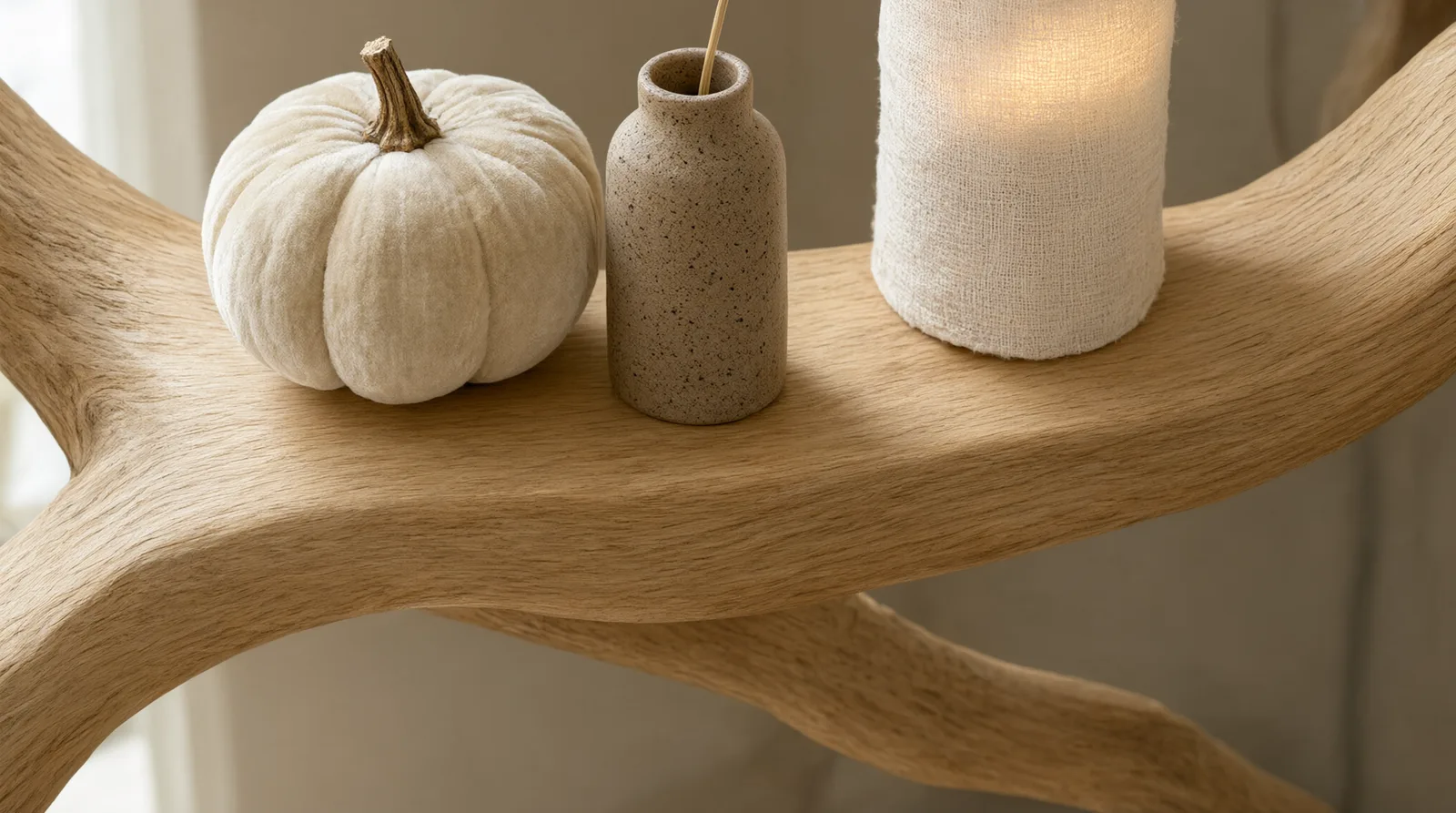 A cream velvet pumpkin, stoneware vase, and glowing candle styled on the branch of a light wood tree bookshelf for an elevated, budget-frien